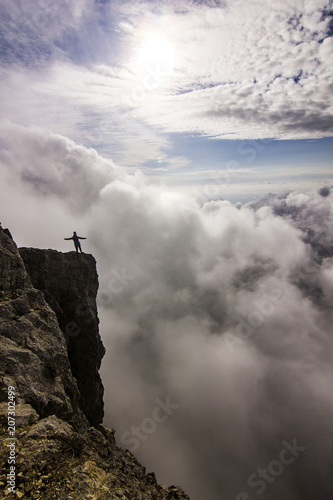 girl with hands up standing on a cliff in clouds