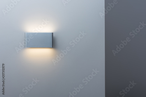 A glowing modern aluminum led lamp on the gray wall. Free space and a darker stripe