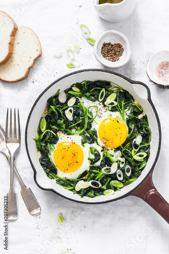 Green shakshuka. Fried eggs with fresh spinach, ramson, leek in a cast iron skillet on a white background, top view