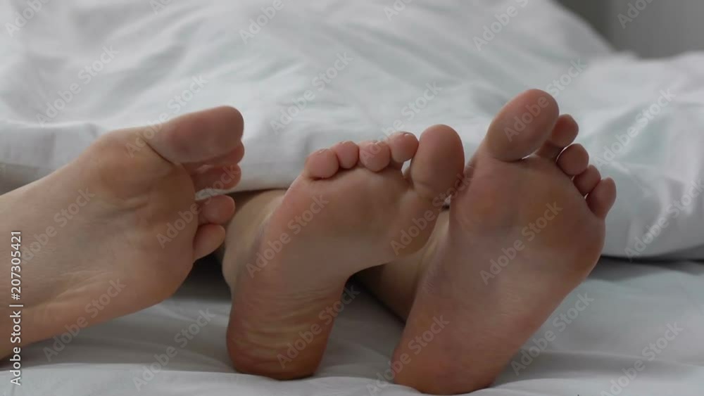 Couple flirting in bed, male touching female leg, relationship and intimacy Couple flirting in bed, male touching female leg, relationship and intimacy