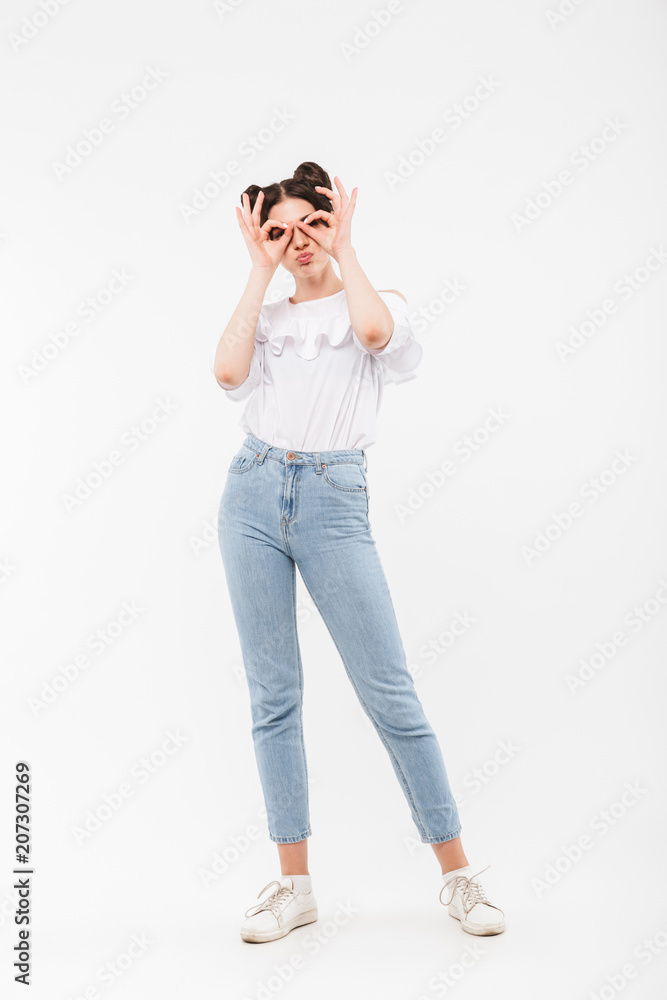 Full length portrait of funny cheerful girl 20s with two buns hairstyle looking at you through binoculars making with fingers, isolated over white background in studio Full length portrait of funny cheerful girl 20s with two buns hairstyle looking at you through binoculars making with fingers, isolated over white background in studio