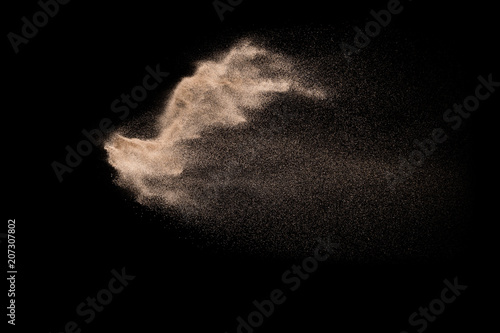 Golden sand explosion isolated on black background. Abstract sand cloud. Golden colored sand splash against dark background. Yellow sand fly wave in the air. photo