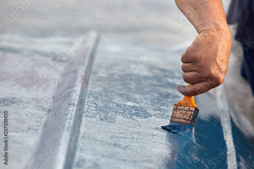 Man painting boat.Closeup view of hand holding a paintbrush with blue color.
