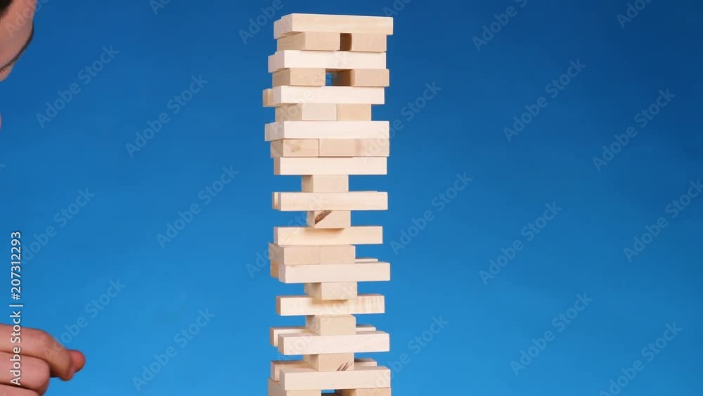 hands of Young man plays jenga on blue background, close-up. A man builds a tower of blocks while playing jenga