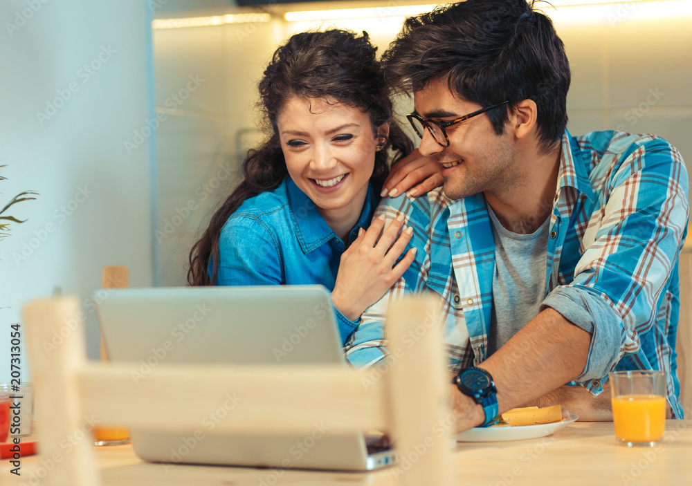 Young couple sitting by table in their apartment and looking at laptop. Young couple sitting by table in their apartment and looking at laptop.
