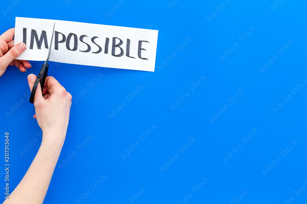 All is possible concept. Hands cutting the part im of written word impossible by sciccors. Blue background top view copy space All is possible concept. Hands cutting the part im of written word impossible by sciccors. Blue background top view copy space