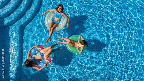 Aerial top view of family in swimming pool from above, happy mother and kids swim on inflatable ring donuts and have fun in water on family vacation, tropical holidays on resort
