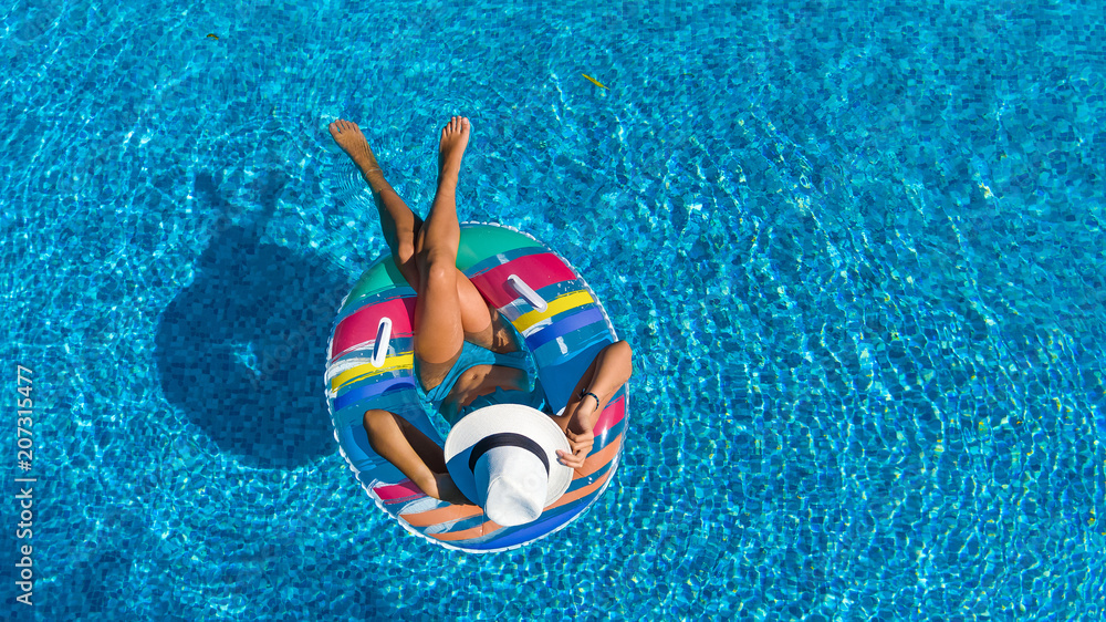 Aerial top view of beautiful girl in swimming pool from above, relax swim on inflatable ring donut and has fun in water on family vacation, tropical holiday resort
