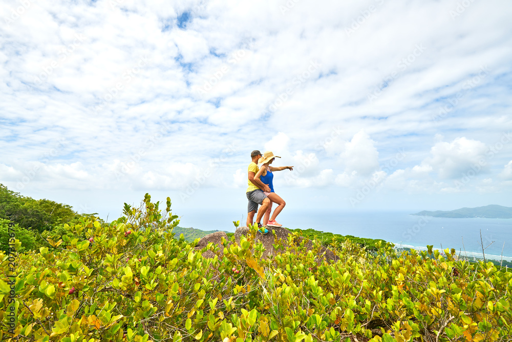 Young couple in love looking at sea and islands from the top of island Seychelles / Highest point from La Digue Island , Nid D'Aigle / Young couple being affectionate on exotic island in vacation Young couple in love looking at sea and islands from the top of island Seychelles / Highest point from La Digue Island , Nid D'Aigle / Young couple being affectionate on exotic island in vacation