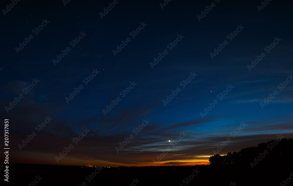Venus in the night sky with stars. A bright sunset with clouds. Cosmic space above the earth's surface. Long exposure.