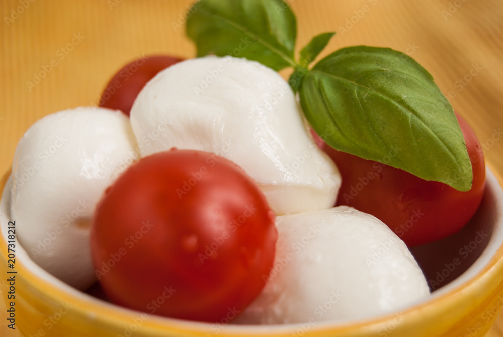 Bowl with little mozzarella tomatoes and leaves of basil Bowl with little mozzarella tomatoes and leaves of basil