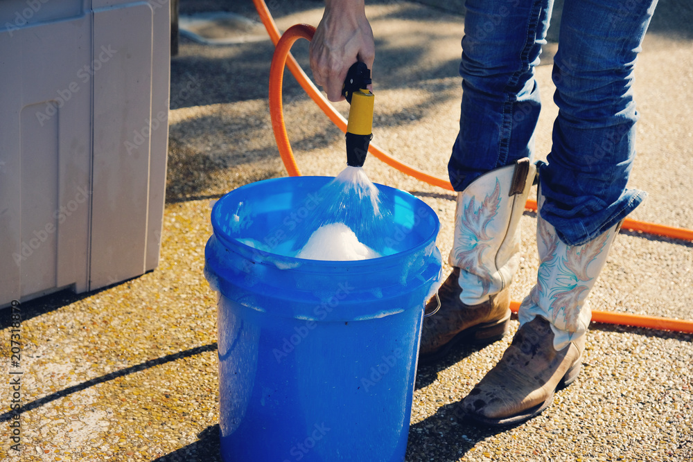 Woman spraying hose into blue bucket during summer to wash. Woman spraying hose into blue bucket during summer to wash.