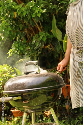 Ein Mann grillt im Garten am Kugelgrill Fleisch und Gemüse