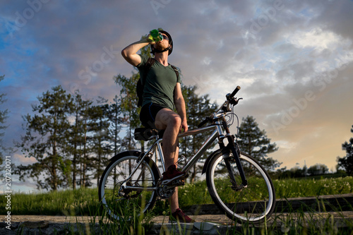Young man sitting on his bike in nature,and drinking water