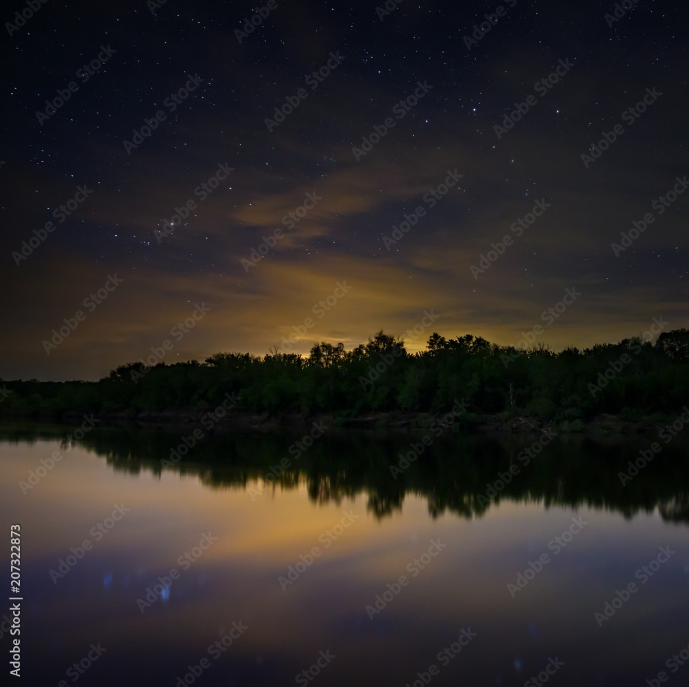 Obraz premium Space with stars in the night sky. The landscape with the river and trees is photographed on a long exposure.