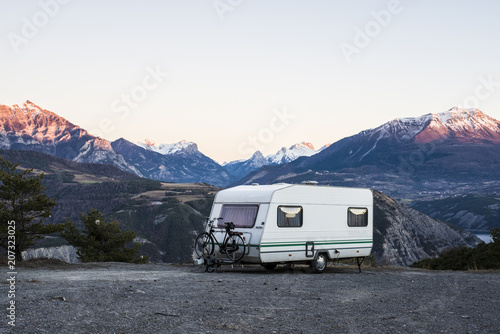 Caravan with a bike parked on a mountaintop with a view on the french Alps near lake Lac de Serre-Poncon
