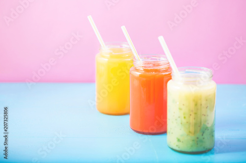 freshly squeezed fruit juice, smoothies yellow orange green on bright blue and pink background Copy space