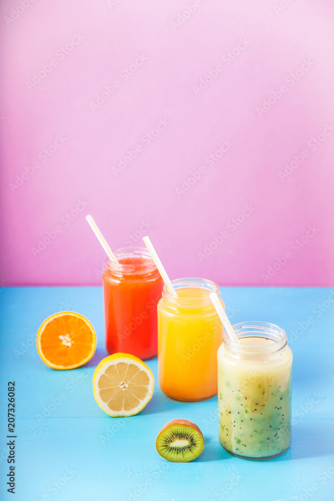 freshly squeezed fruit juice, smoothies yellow orange green lemon apple orange kiwi on bright blue and pink background Copy space. freshly squeezed fruit juice, smoothies yellow orange green lemon apple orange kiwi on bright blue and pink background Copy space.