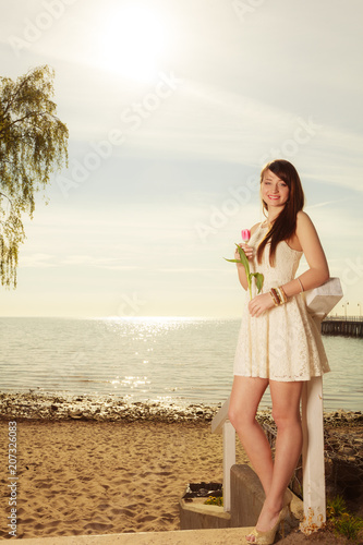 Woman standing on beach holding pink tulip