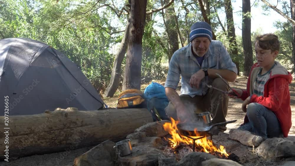 Father and son cooking over a fire on a camping trip together in nature Father and son cooking over a fire on a camping trip together in nature