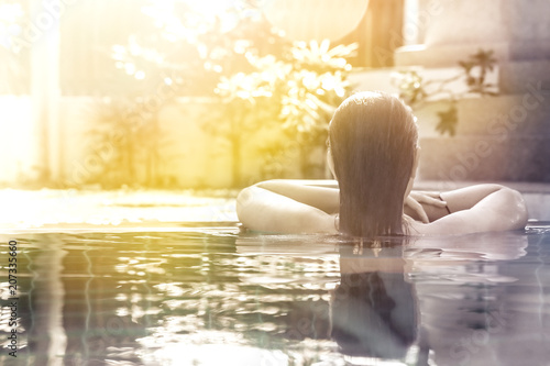 woman relaxing in hotel spa swimming pool looking at view with sunlight and copy space