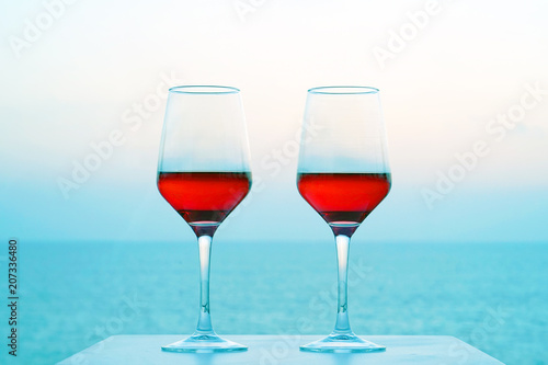Two glasses of red wine on a background of sea horizon morning. Two glasses of red wine with blue sea in background. Two Glasses of Red Wine Standing on Table at the hotel balcony.