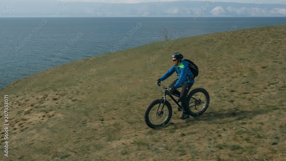 Fototapeta premium Fat bike also called fatbike or fat-tire bike in summer driving through the hills. The guy is riding a bike along the sand and grass high in the mountains. He performs some tricks and runs dangerously