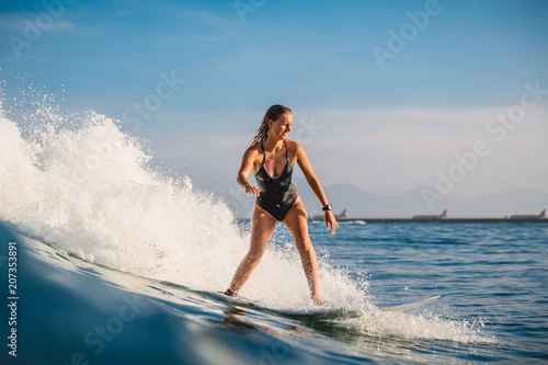 Surfer woman at surfboard ride on ocean wave. Woman in ocean during surfing. Bali, Airport © artifirsov