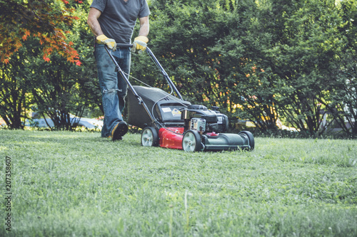 Red lawn mower cutting grass being pushed across a residential lawn 