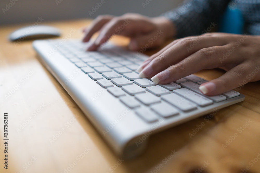 Close up image of female hands typing text on a wireless keyboard. Business woman working at the office. On wooden table Close up image of female hands typing text on a wireless keyboard. Business woman working at the office. On wooden table