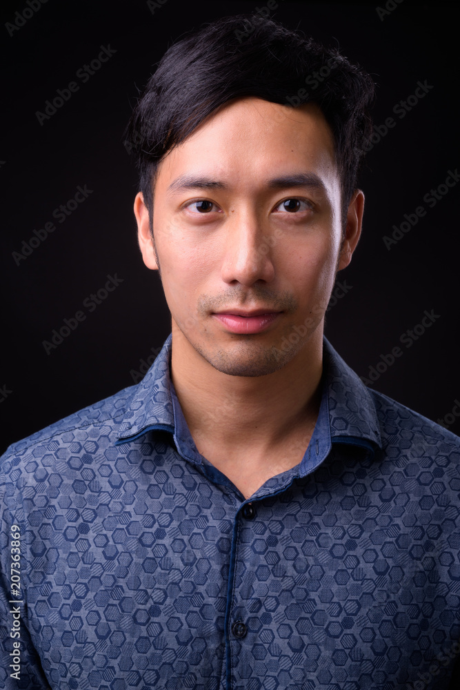 Young handsome Asian businessman against black background