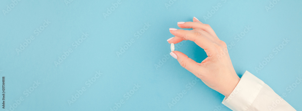 Female hand holding a white pill - obrazy, fototapety, plakaty 