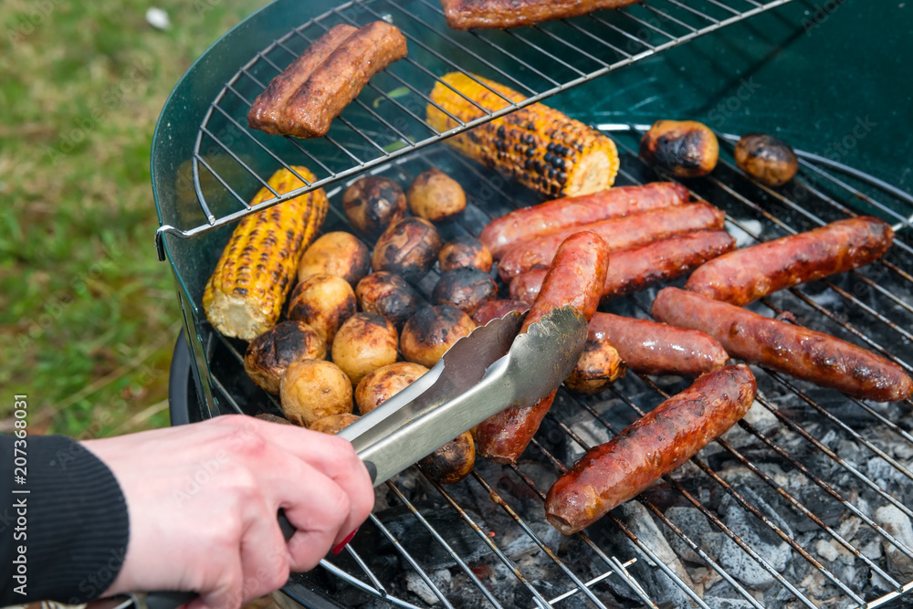 Baked potatoes, corn and sausages on a barbecue grill