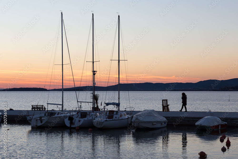 An harbour on a lake at sunset, with various boats and a woman t
