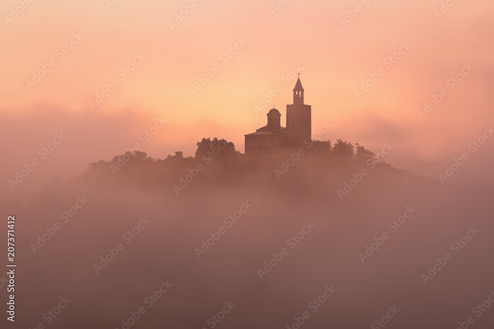 Amazing beautiful view over Tsarevets Fortress in Veliko Tarnovo, Bulgaria on a foggy sunrise in summer.