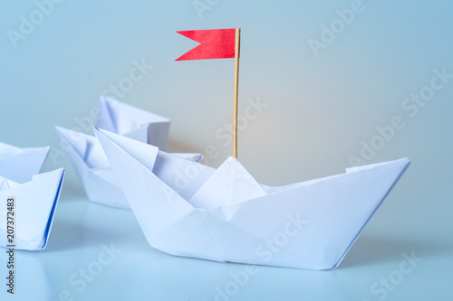 Leadership concept using  paper ship with red flag on blue background