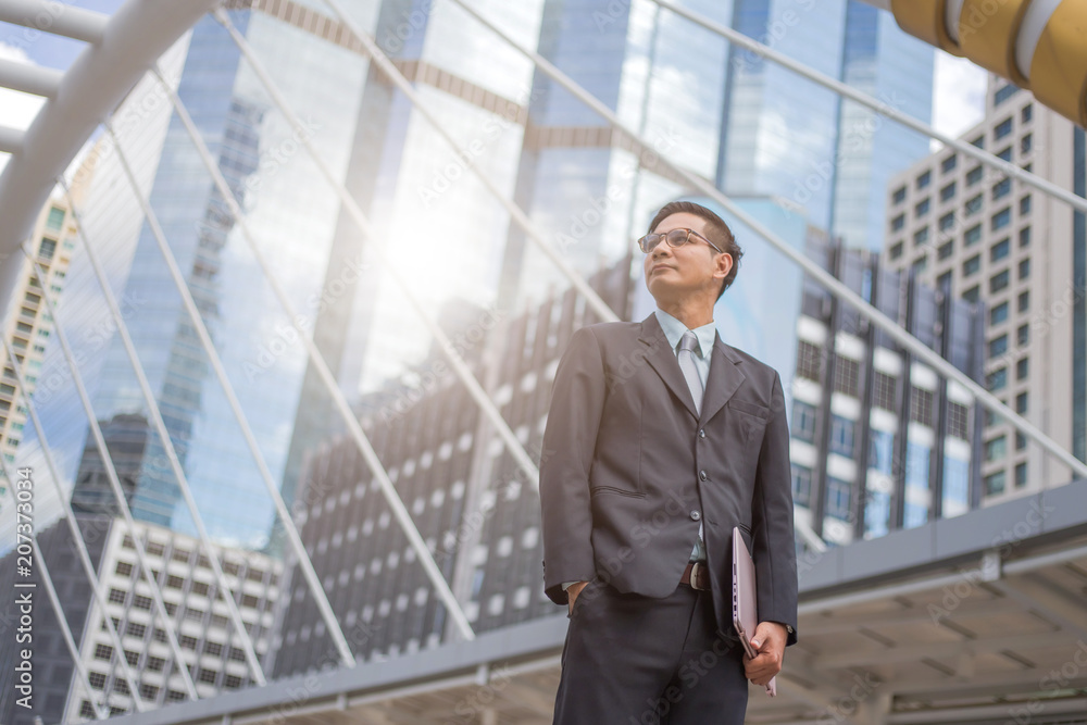 Young Asia businessman in suit with his laptop computer outdoors, modern building on the background Young Asia businessman in suit with his laptop computer outdoors, modern building on the background