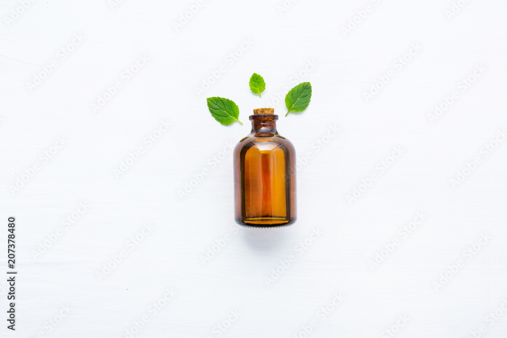 Natural Mint Essential Oil in a Glass Bottle with Fresh Mint Leaves on white wooden background. Natural Mint Essential Oil in a Glass Bottle with Fresh Mint Leaves on white wooden background.