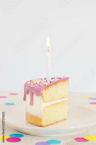Trozo de pastel de cumpleaños con una vela sobre fondo blanco con confeti