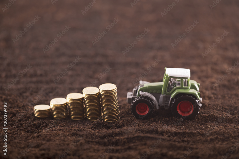 Fototapeta premium Tractor miniature with coins on fertile soil land