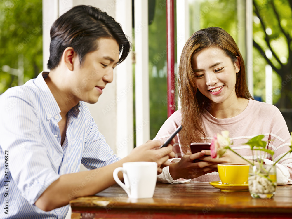 young asian couple playing with cellphone in coffee shop or tea house young asian couple playing with cellphone in coffee shop or tea house