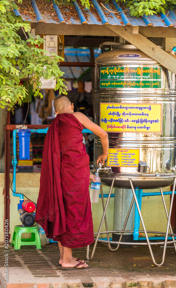 BAGAN, MYANMAR - DECEMBER 1, 2016: Monk near the barrel of water. Vertical.