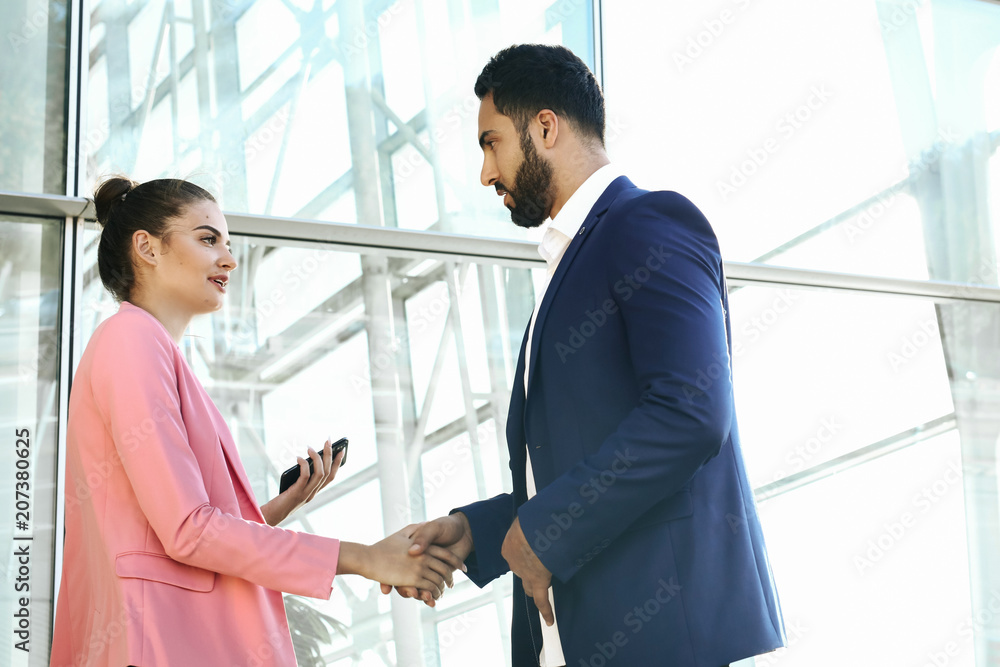 Welcome on board! Two handsome men shaking hands with smile while sitting on the couch at office with their coworkers Welcome on board! Two handsome men shaking hands with smile while sitting on the couch at office with their coworkers