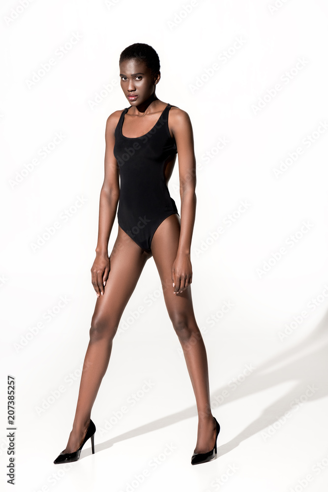 full length view of beautiful african american girl in bodysuit and high heeled shoes looking at camera on white full length view of beautiful african american girl in bodysuit and high heeled shoes looking at camera on white