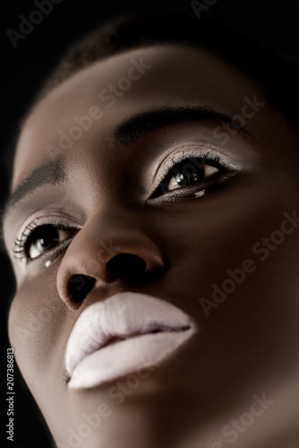 low angle view of beautiful african american girl with white lips looking away isolated on black