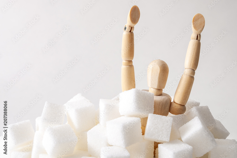 Sugar addiction, insulin resistance, unhealthy diet and November 14 is diabetes awareness day concept with a puppet drowning in sugar cubes isolated on white background and copy space for text