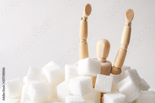 Sugar addiction, insulin resistance, unhealthy diet and November 14 is diabetes awareness day concept with a puppet drowning in sugar cubes isolated on white background and copy space for text photo