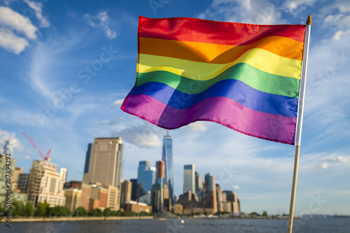 Colorful rainbow gay pride flag fluttering in the breeze against a sunny city skyline 