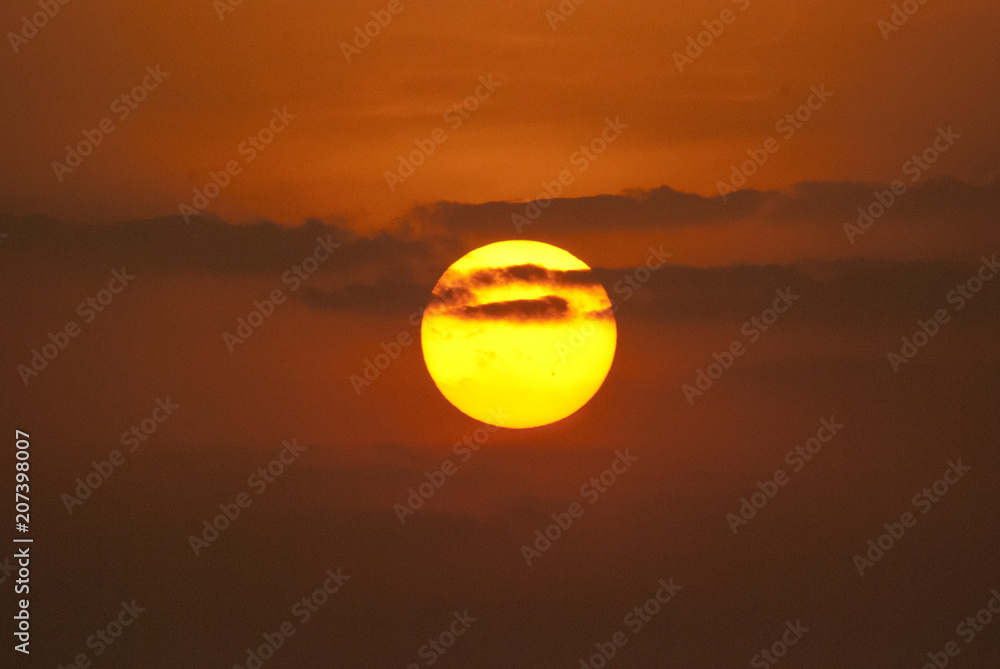 A setting sun behind clouds with orange colour