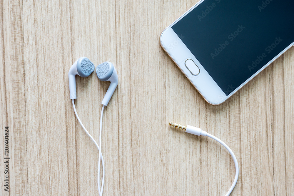 White earphones with smartphone on office wooden desk background. White earphones with smartphone on office wooden desk background.